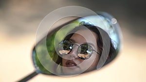 Lady with brown hair in sunglasses reflects in bike mirror