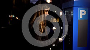 Lady buying ticket from parking payment machine at night, crime risk, danger