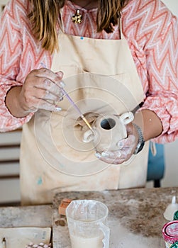 Lady ceramic artist working in her studio interior, woman`s hands painting objects