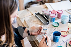 Lady ceramic artist working in her studio interior, woman`s hands painting objects