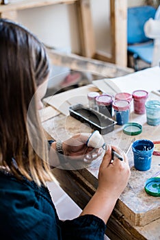 Lady ceramic artist working in her studio interior, woman`s hands painting objects