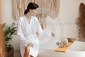 Lady Choosing Cosmetics On Shelf Sitting On Bathtub In Bathroom