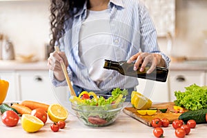 Lady cooking fresh vegetable salad, adding olive oil and seasoning to bowl, enjoying eating healthy vegetarian food