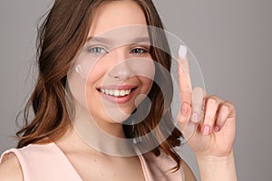 Lady with cream showing one finger. Close up. Gray background