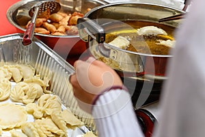 Lady deep frying traditional Chinese Yau Kok Zai or sweet dumpling with some raw ones nearby for Chinese New Year