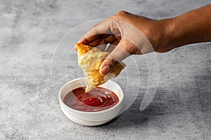 a lady dipping Samosa on tomato sauce. Indian street food.