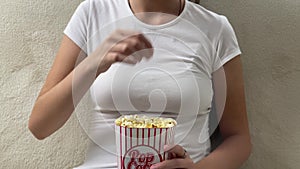 Lady eating popcorn while looking at TV screen