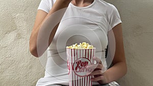 Lady eating popcorn while looking at TV screen