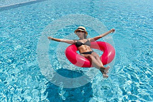 A lady enjoy a sunny day, floating on a bright inflatable ring in a clear blue swimming pool