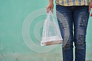 lady in fashionable ripped jeans stands in light green wall. woman taking a plastic bag of packed lunch.