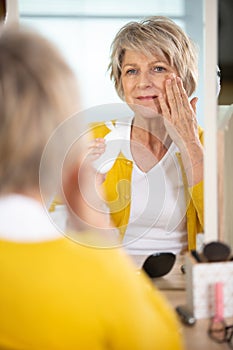 lady in fifties applies skincare product to face