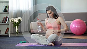 Lady in final stages of pregnancy doing yoga, drinking water, safe childbirth