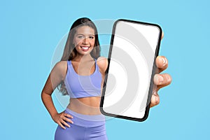 lady in fitwear showcasing large phone with empty screen, studio