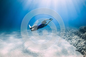Lady free diver in swimsuit posing underwater at the deep in blue sea with sunlight