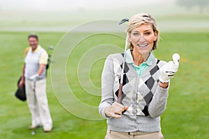 Lady golfer smiling at camera with partner behind