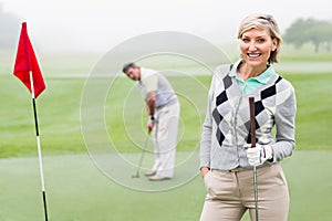 Lady golfer smiling at camera with partner behind