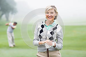 Lady golfer smiling at camera with partner behind