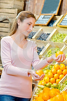 Lady in greengrocers holding orange in each hand