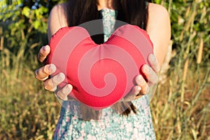 Lady hands gently raise and hold red heart with love and respect with background of nature