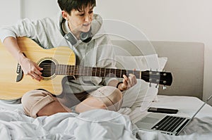 Lady in headphones is reading chords from the screen of laptop and playing on acoustic guitar