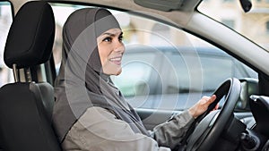 Lady in hijab looking rear view mirror sitting in auto, city transport, license