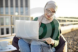 Lady in hijab putting charge cable into laptop outdoors