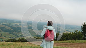 Lady hiker with backpack looking on hills and mountains