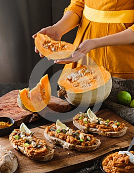 Lady holding fresh pumpkin next to toasted bread bruschetta with vegetable caviar, made of squash, pumpkin served with green