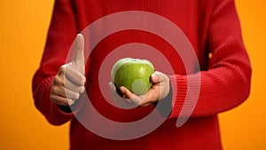 Lady holding green apple hand showing thumbs up, fruit snack, healthy nutrition