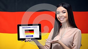 Lady holding tablet with learn German app, Germany flag on background, education