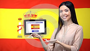 Lady holding tablet with learn Spanish app, Spain flag on background, education photo