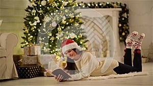 Lady with Long Hair holding an Opened Book in Her Hands and Smiling on Xmas Tree Background. Pretty Brunette with Santa