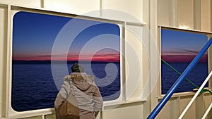 Lady looking through the scuttle while Irish ferry is leaving Cherbourgh in France to Dublin harbour during sunset -