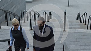 Lady and male partners walking on staircase near office building, cooperation