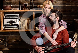 Lady and man with beard on dreamy faces hugs and plays guitar. Couple in wooden vintage interior enjoy guitar music