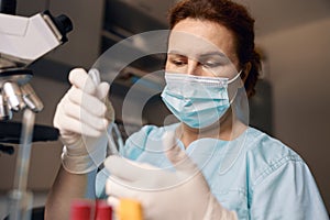 Lady in medical mask and gloves takes liquid from test tube conducting experiment at workplace