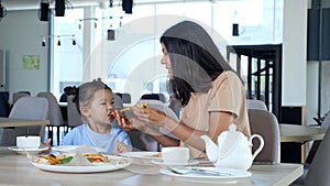 Lady mom holds pizza slice and daughter eats in cafe