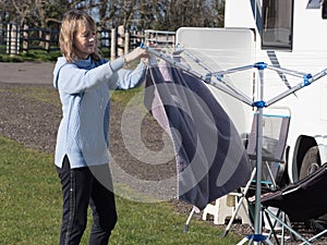 A lady motorhome owner hangs her towel on a rotary hair dryer with her recreational vehicle in the background.Sunny