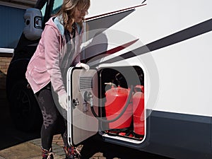A lady motorhome owner opens a gas locker door wearing gloves.LPG gas bottles can be seen.