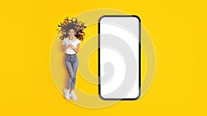 Lady Near Huge Cellphone Listening Music Using Phone, Yellow Background