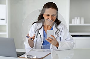 Lady physician working online from clinic, using phone