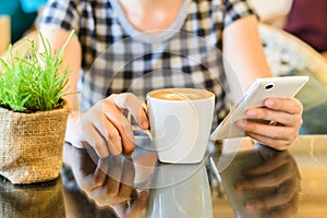 A lady picking up a cup of coffee at a coffee shop with reflections as she sits at a table