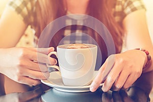 A lady picking up a cup of coffee at a coffee shop with reflections as she sits at a table