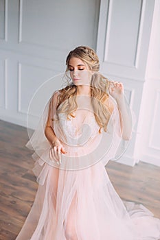 Lady in pink luxurious light dress in spacious room with white walls and bright light, gentle lace peignoir and veil