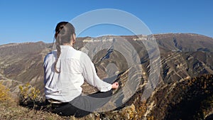 Lady with plait meditates on cliff against distant mountains