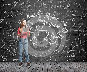 Lady is pondering about complicated math problem. Formulas and graphs are drawn on the black chalk wall.