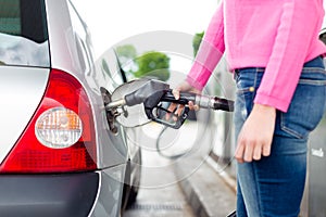 Lady pumping gasoline fuel in car at gas station.