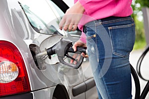 Lady pumping gasoline fuel in car at gas station.
