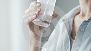 Lady putting aspirin tablet into glass of water, drinking painkiller medicine