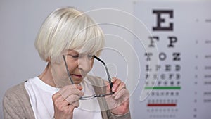 Lady retiree putting on spectacles, smiling and reading on smartphone, blindness